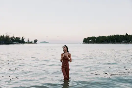 Молодая женщина в платье стоит по грудь в спокойной воде на фоне островов
