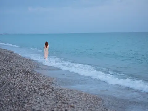 Женщина в свитере стоит у океана на фоне голубого неба и чистой воды
