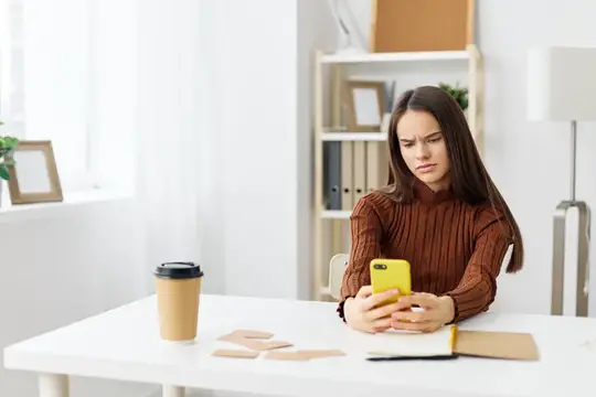 Недовольная девушка с телефоном за рабочим столом