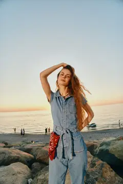 Молодая женщина с рыжими волосами на каменистом берегу на закате