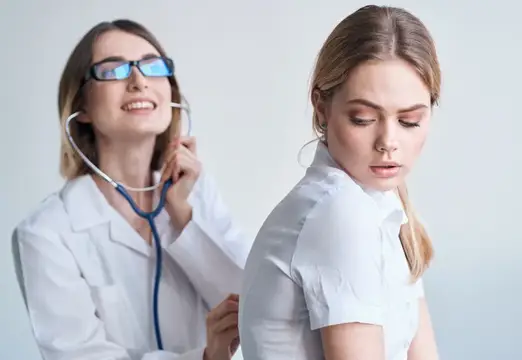 Женщина-врач в очках слушает пациентку стетоскопом