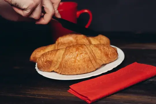 Рука нарезает ножом свежие круассаны на завтрак