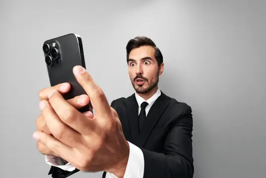 Удивлённый мужчина в костюме делает селфи на смартфон
