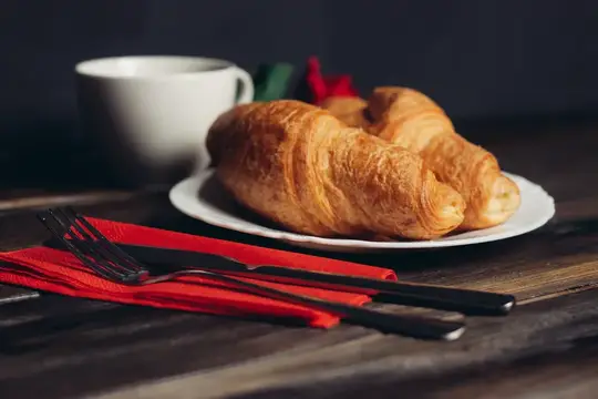 Свежие круассаны на тарелке с чашкой кофе и красной салфеткой