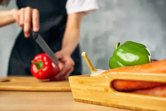 Повар нарезает красный перец на кухонной доске