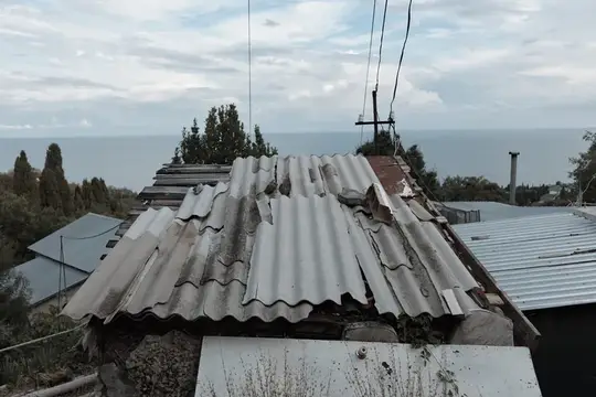 Старая крыша из волнистого шифера на фоне моря и неба