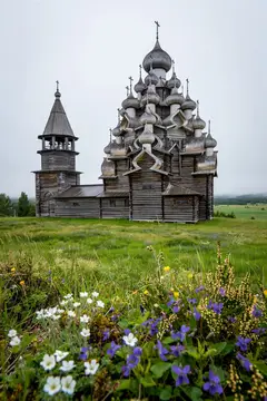 Старинная деревянная церковь с куполами на фоне летнего луга