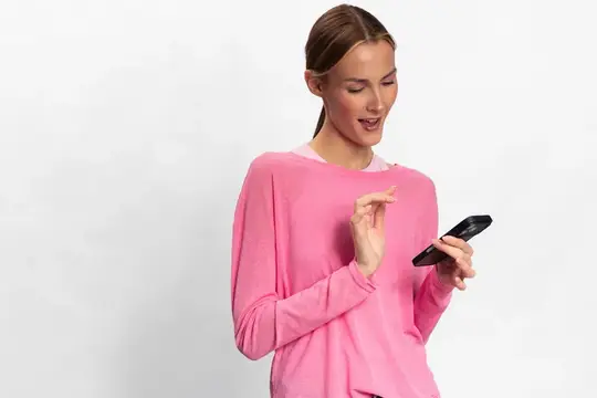 Удивлённая девушка в розовом свитере смотрит на смартфон