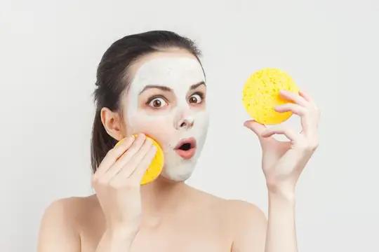 Удивлённая девушка с глиняной маской на лице и жёлтыми спонжами