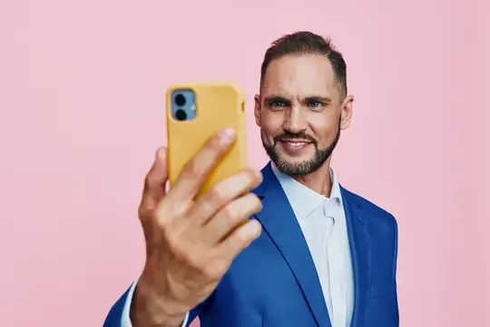 Улыбающийся мужчина в синем пиджаке делает селфи на жёлтый смартфон