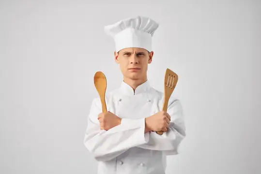 Весёлый мужчина-шеф-повар на кухне занимается приготовлением пищи
