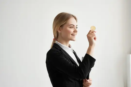 Улыбающаяся блондинка в деловом костюме рассматривает монету