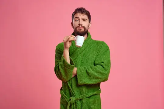 Мужчина с чашкой чая на розовом фоне, обрезанный вид, модель в зелёном халате