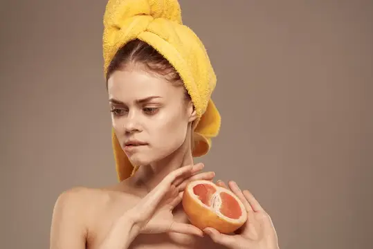 Симпатичная женщина с обнажёнными плечами держит в руке грейпфрут