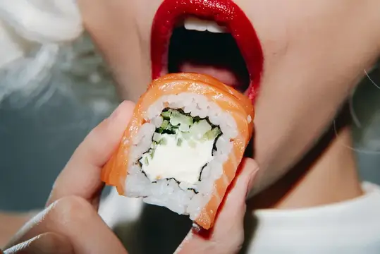 Модная модель с яркой красной помадой откусывает вкусный ролл с суши с лососем и огурцом, идеально подходит для любителей еды