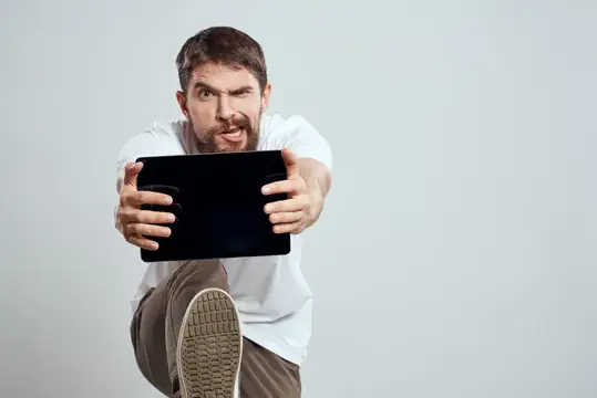 Разъяренный мужчина с планшетом тянется к камере на сером фоне