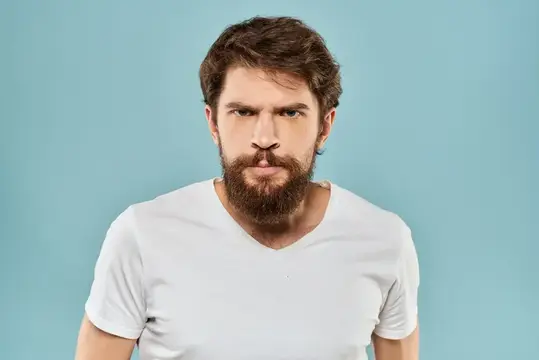Бородатый мужчина в белой футболке смотрит прямо на голубом фоне