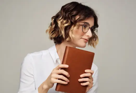 Молодая женщина в очках с книгой в руках на сером фоне