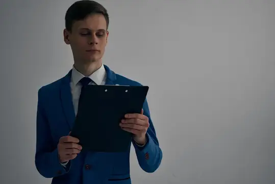 Молодой человек в синем костюме сосредоточенно читает документы на планшете