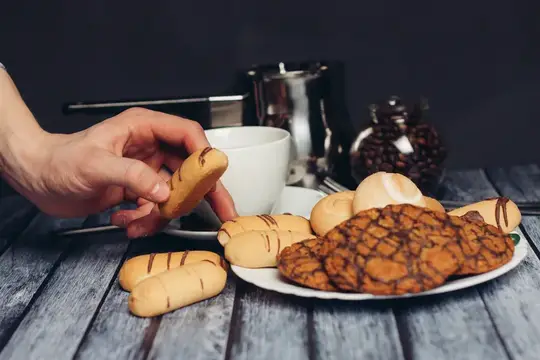 Рука берет печенье с тарелки рядом с чашкой кофе