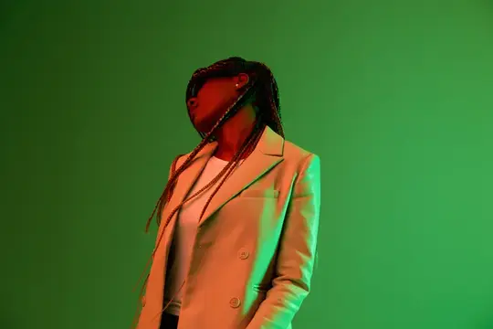 Темнокожая девушка с косичками в белом пиджаке на зелёном фоне