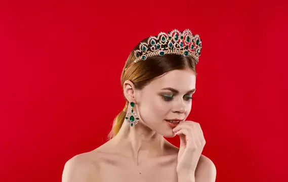 Молодая женщина в диадеме с изумрудами на красном фоне