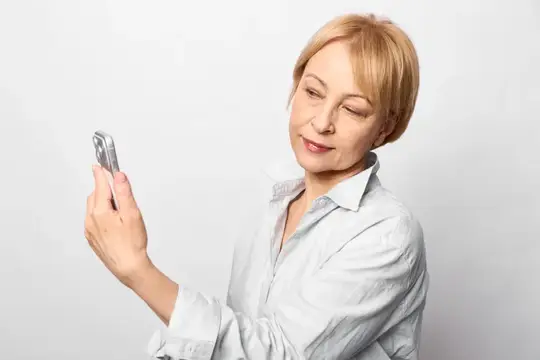 Светловолосая женщина смотрит в смартфон на светлом фоне