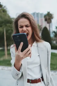 Разъяренная женщина в белом пиджаке кричит на смартфон на улице