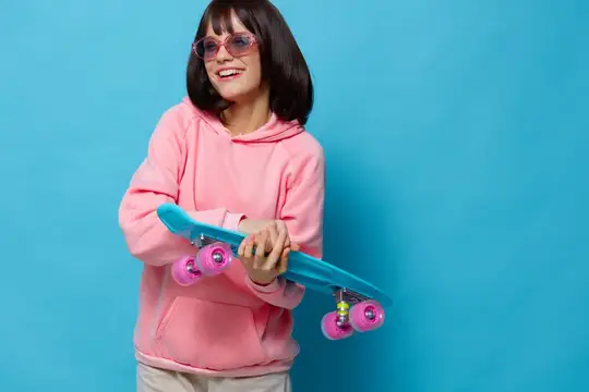 Улыбчивая девушка в розовом худи держит голубой скейтборд