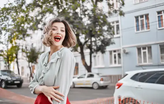Смеющаяся кудрявая девушка в блузе на городской улице