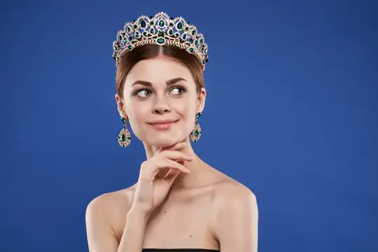 Молодая женщина в роскошной короне с изумрудами на синем фоне