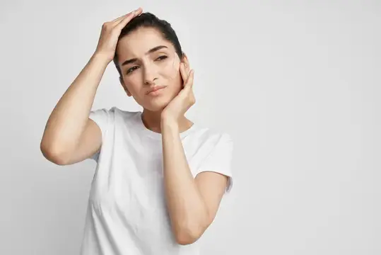 Молодая женщина с закрытыми глазами поправляет волосы на светлом фоне