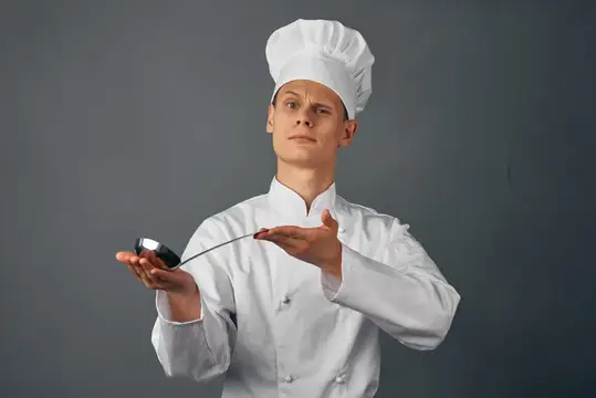Молодой повар в белом колпаке жестом показывает на продукт