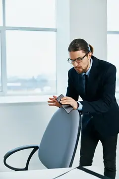 Мужчина в очках и костюме со смартфоном у окна в офисе