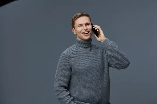 Улыбающийся светловолосый мужчина в свитере говорит по телефону