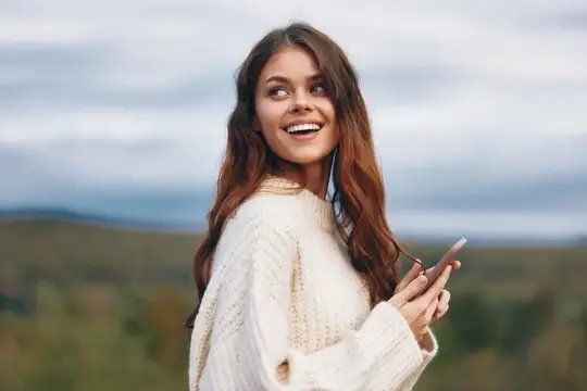 Улыбающаяся шатенка со смартфоном на фоне холмов