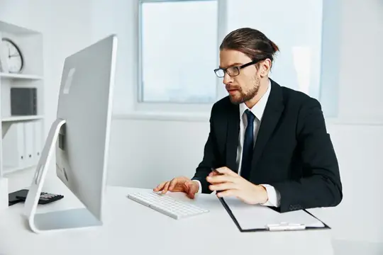 Мужчина в очках и деловом костюме работает за компьютером в офисе