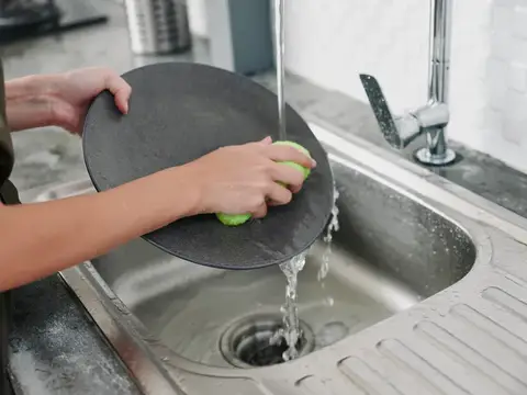 Женщина моет тёмную тарелку под струёй воды в раковине