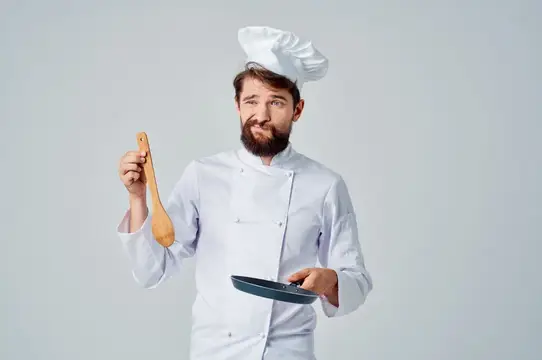 Бородатый повар в колпаке с деревянной ложкой и сковородой