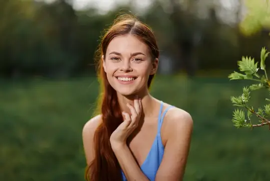 Рыжеволосая девушка улыбается на фоне зелёного парка