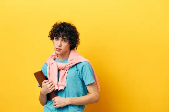 Парень с книгой, студент колледжа, в розовой куртке на желтом фоне
