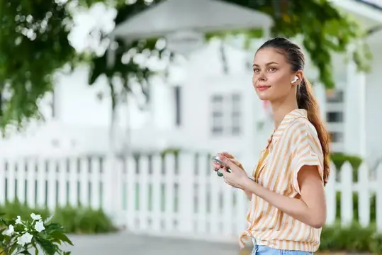 Молодая женщина в наушниках на фоне белого забора