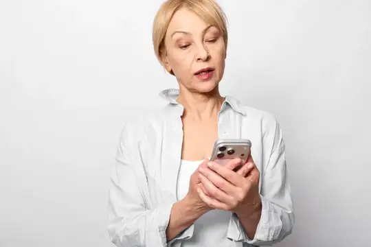 Пожилая женщина со смартфоном в руках, снятая крупным планом в помещении на студийном белом фоне