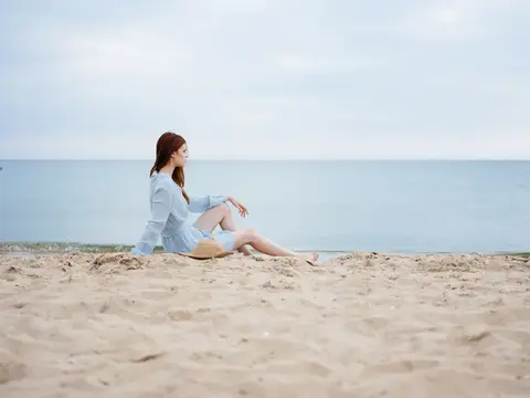 Молодая женщина сидит на песчаном пляже у моря в пасмурный день