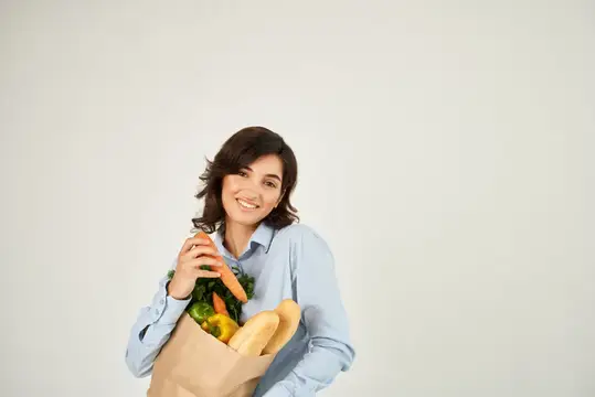 Улыбающаяся брюнетка с бумажным пакетом овощей и багетом