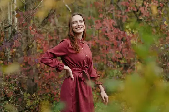 Улыбающаяся женщина в бордовом платье осенью в лесу