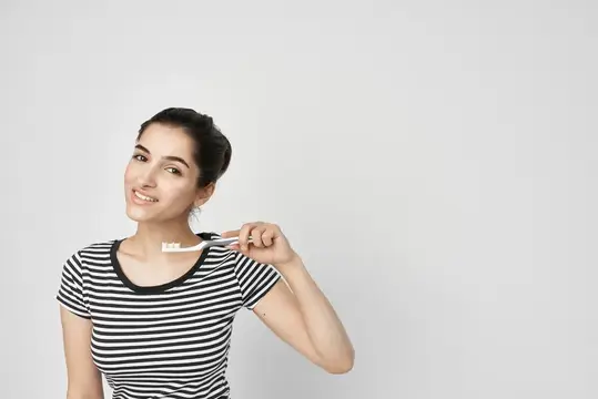 Улыбающаяся темноволосая девушка с зубной щеткой на белом фоне