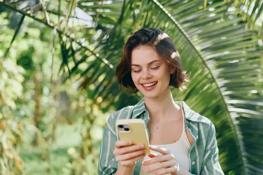 Улыбающаяся девушка с телефоном в тропическом саду
