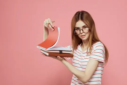 Молодая студентка с книгами на розовом фоне, в очках, крупный план лица