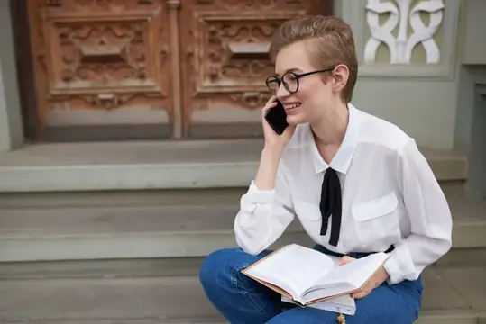 Улыбающаяся девушка с короткой стрижкой говорит по телефону на ступеньках